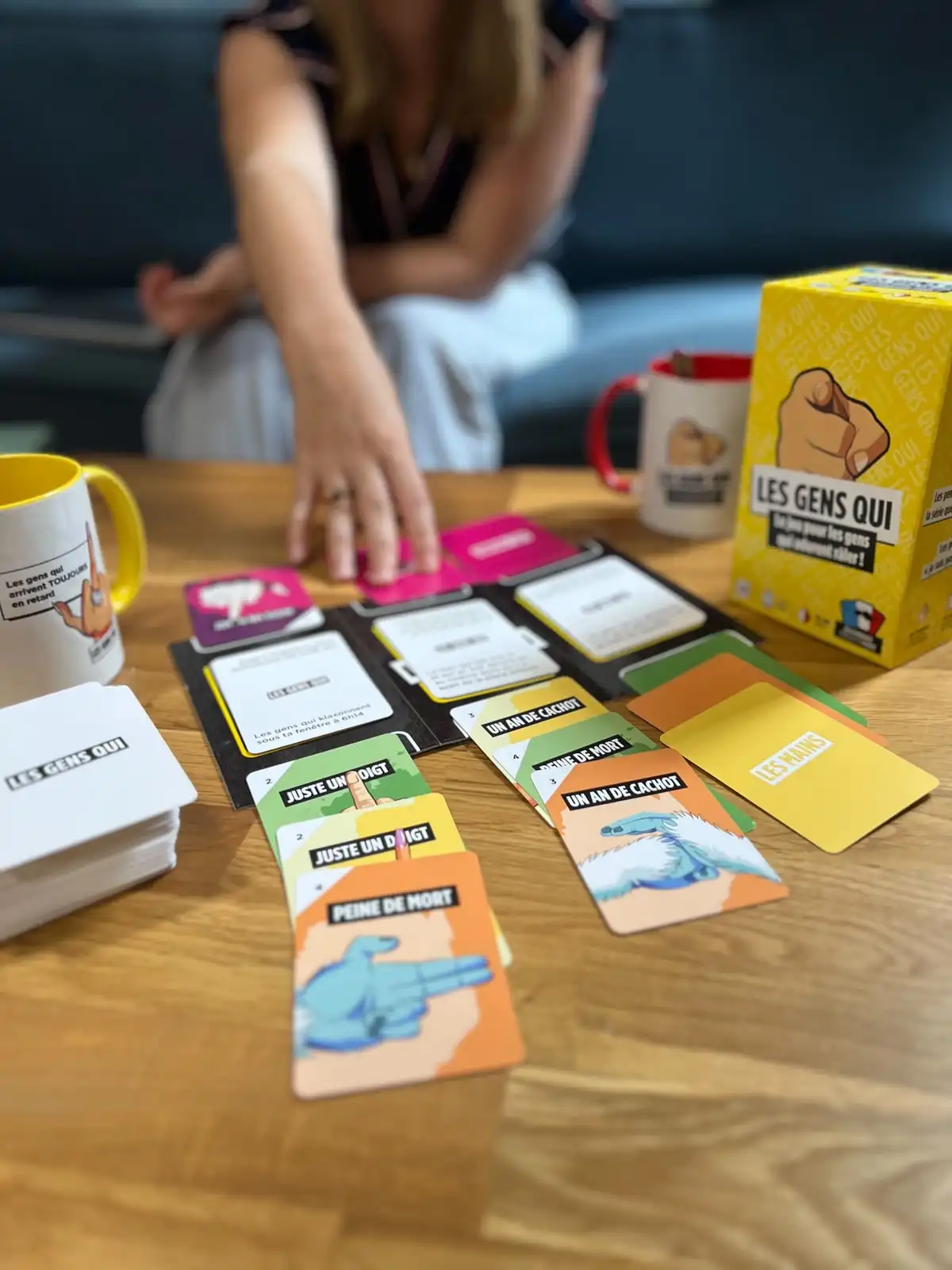 Une joueuse sur un canapé tend la main vers les cartes Mains posées sur la table basse, la boîte à côté
